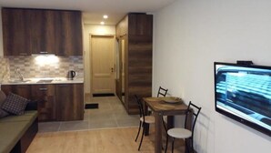 A compact living space with a kitchenette, dining area, and a TV mounted on the wall. - New Gudauri Block 4 - Ski4Life (Kazbegi)