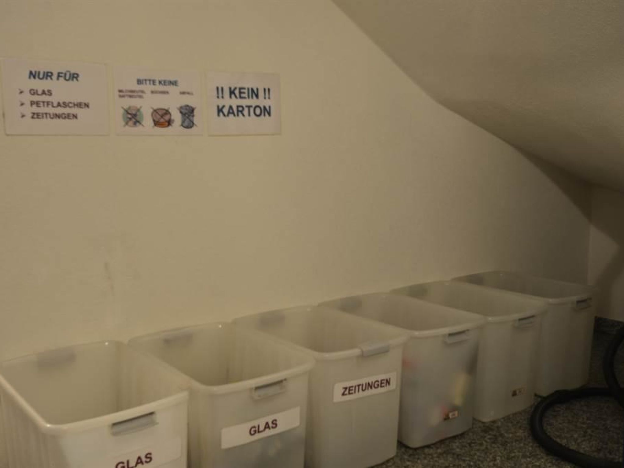 Una hilera de contenedores etiquetados en una habitación, incluyendo contenedores para vidrio, periódicos y uno específicamente para no usarlos.
