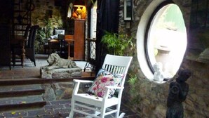 Ein rustikales Steinhaus mit einem weißen Schaukelstuhl, floralen Kissen, einer Löwenstatue und einem runden Spiegel an der Wand.