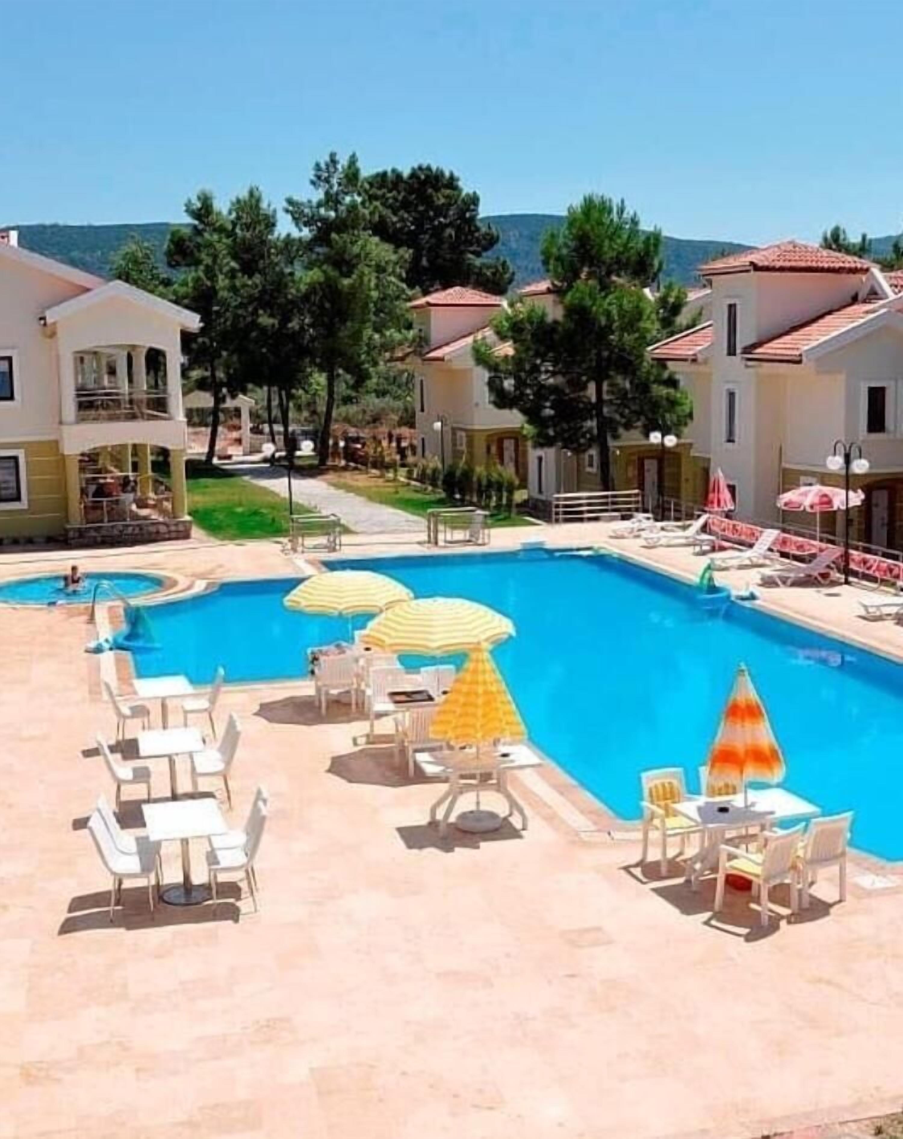 A pool area with lounge chairs and umbrellas, surrounded by buildings with red-tiled roofs.