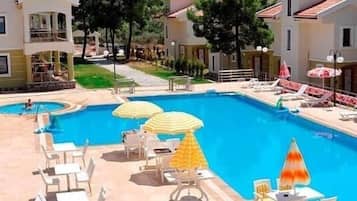 A pool area with lounge chairs and umbrellas, surrounded by buildings with red-tiled roofs.
