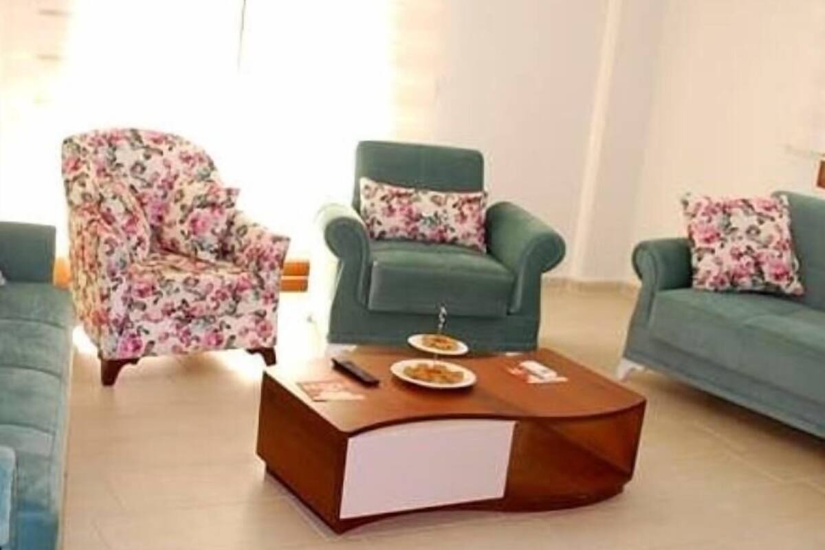 Una sala de estar con dos sofás verdes, uno con funda de estampado floral, y una mesa de centro de madera con un control remoto y un plato de comida.