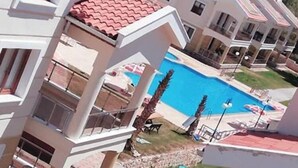 Un resort con varias construcciones, piscina y montañas al fondo.