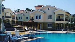 Una piscina con sillas de descanso y sombrillas, rodeada de edificios de varios pisos con balcones.