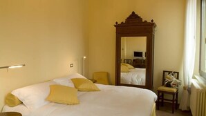 A hotel room with a large bed, a wooden headboard, a mirror, a chair, and a radiator. - Ada Bed and Breakfast (Ferrara)