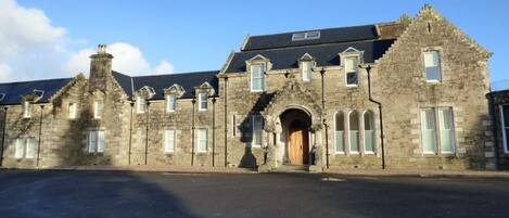 A historic stone building with a central arched entrance, multiple windows, and a flat roof.