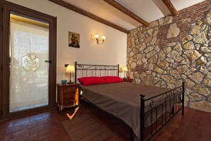 A bedroom with a stone wall, a bed with a metal frame, two bedside tables with lamps, and a door with a frosted glass panel.