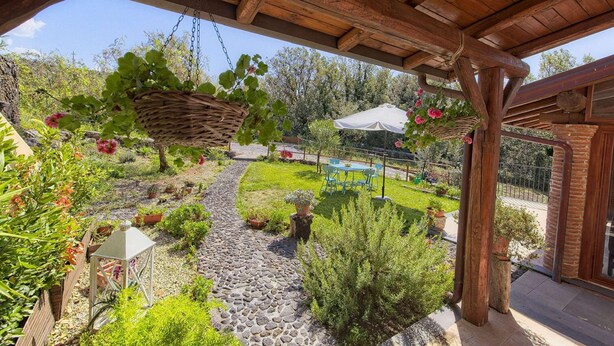 Un patio couvert avec un chemin en pierre, des jardinières suspendues et du mobilier d’extérieur.