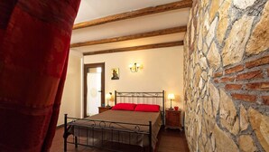 Une chambre avec un mur en pierre, un lit avec des oreillers rouges et deux lampes de chevet.