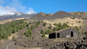 Un petit bâtiment en pierre, doté d’un toit sombre, entouré d’un terrain rocailleux et d’une végétation clairsemée, avec des montagnes en arrière-plan.