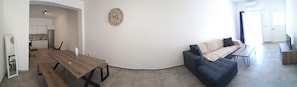 A modern living room with a wooden dining table, a blue sofa, and a wall clock.