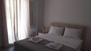 A neatly made bed with white linens and towels, a bedside lamp, and a window with sheer curtains. - Papillon (Astypalaia)