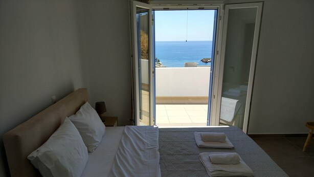 A bedroom with a bed, a nightstand, and a view of the sea through an open door. - Papillon (Astypalaia)