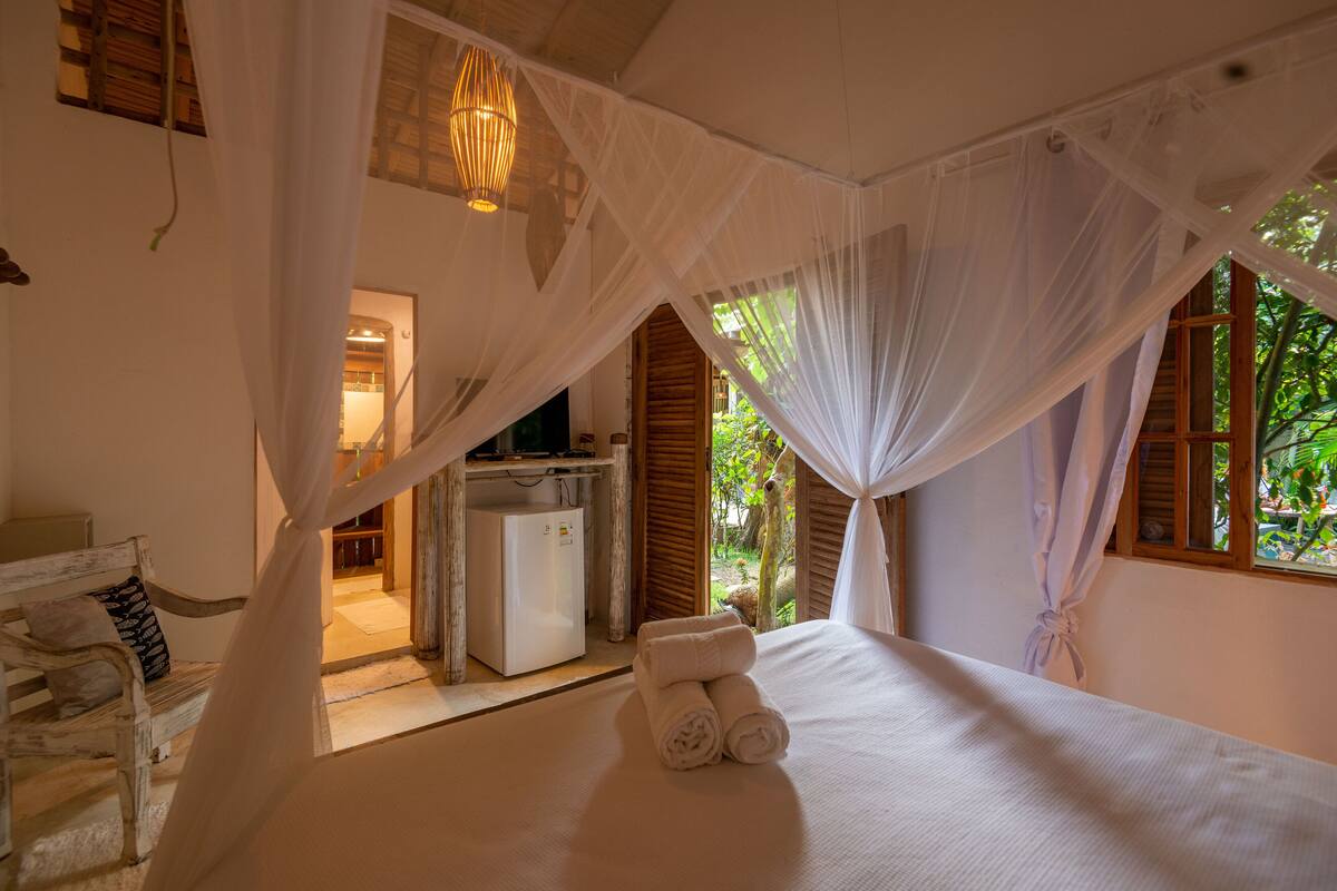A bedroom with a canopy bed, a small kitchenette, and a view of greenery outside.
