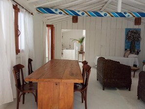 A dining area with a wooden table and chairs, a wicker sofa, and a painting on the wall. - Casa da Gloria (Porto Seguro)