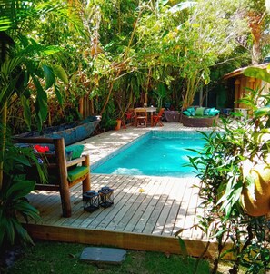 A wooden deck with a swimming pool, surrounded by lush greenery and a wooden fence. - Casa da Gloria (Porto Seguro)