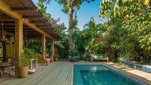 A wooden deck with a pool, surrounded by lush greenery and a wooden pergola. - Casa da Gloria (Porto Seguro)