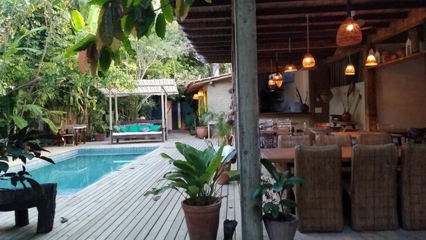 A wooden deck with a pool, outdoor seating, and hanging lights. - Casa da Gloria (Porto Seguro)