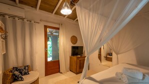 A bedroom with a bed, a television, a wicker chair, and a wooden cabinet. - Casa da Gloria (Porto Seguro)