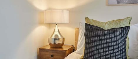 A neatly made bed with a patterned pillow and a lamp on a wooden bedside table.