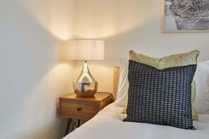 A neatly made bed with a patterned pillow and a lamp on a wooden bedside table. - Host & Stay | Caedmon House (Whitby)