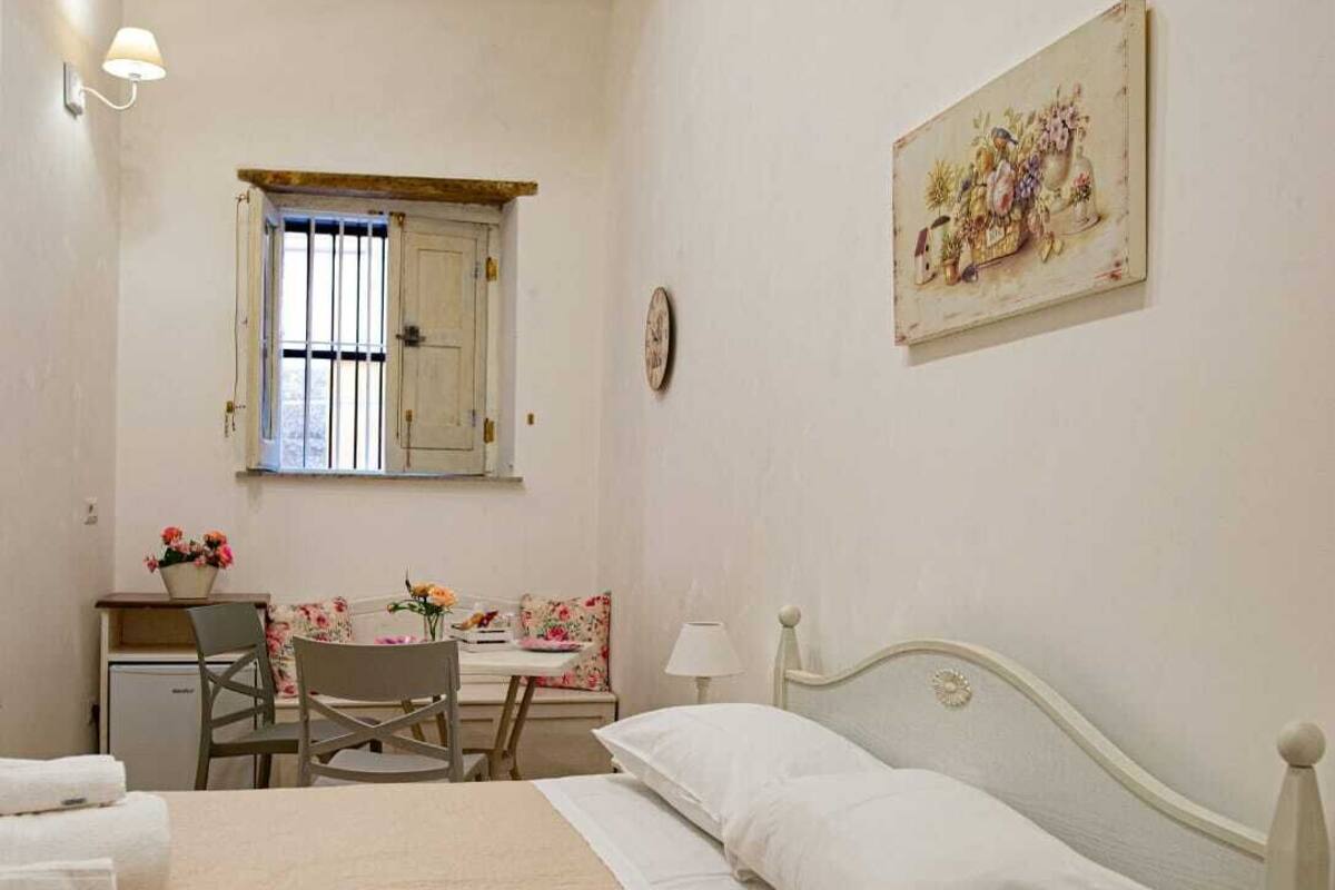 A bedroom with a bed, a desk, a chair, a lamp, a clock, and a painting on the wall.