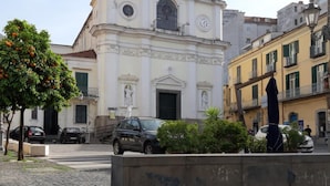 A church with a bell tower, a clock, and a statue in front. - B&B Al Portone (Pagani)