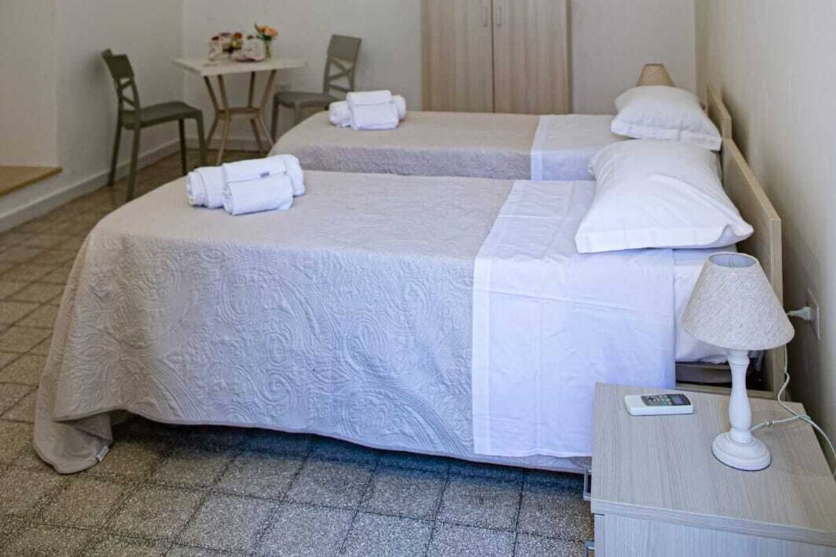 A hotel room with two beds, a chandelier, a desk with chairs, a clock, and artwork on the wall.