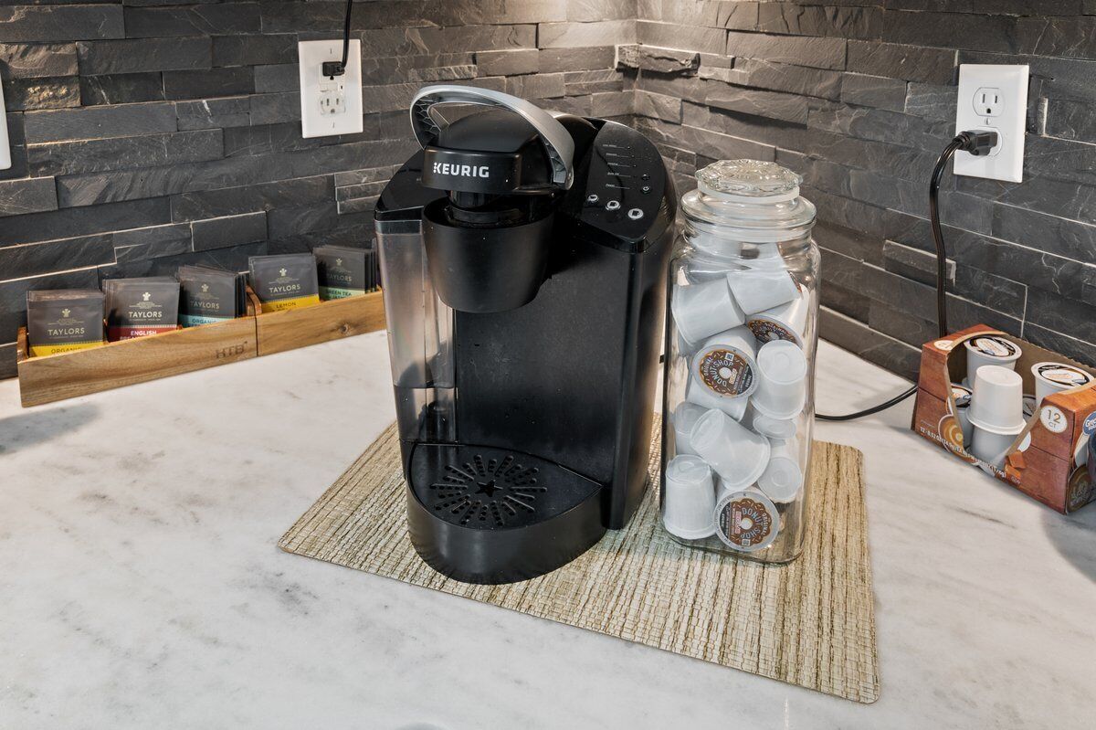 A Keurig coffee maker on a kitchen counter with a coffee bean dispenser and a glass jar of coffee pods.
