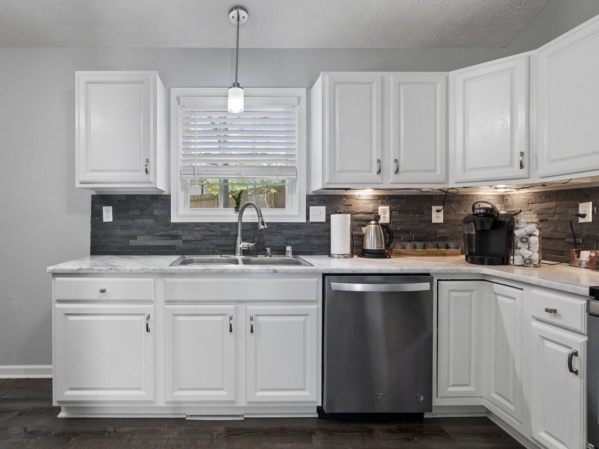 A modern kitchen with white cabinets, a stainless steel dishwasher, and a stone backsplash.