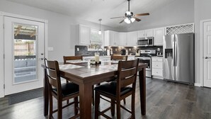 A modern kitchen with white cabinets, stainless steel appliances, a dining table with chairs, and a ceiling fan.