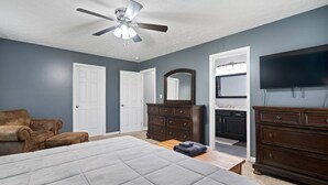 A bedroom with a large bed, a ceiling fan, a TV, and a dresser.