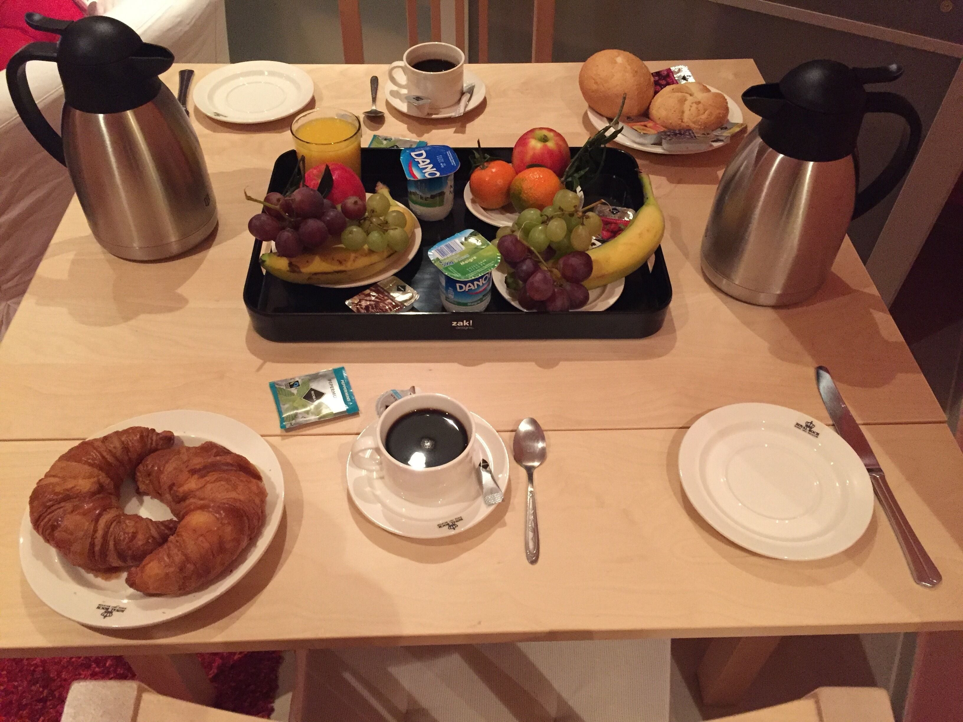 Bandeja de desayuno con frutas, yogur y un croissant sobre una mesa de madera.