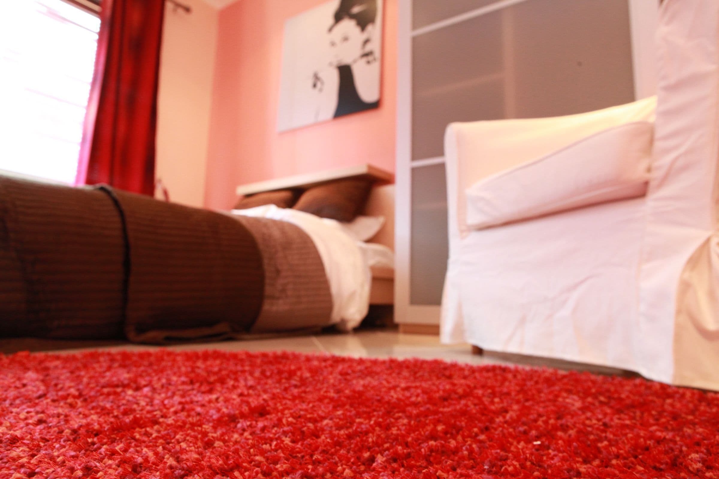 A bedroom with a red carpet, a bed with white bedding, and a white chair.