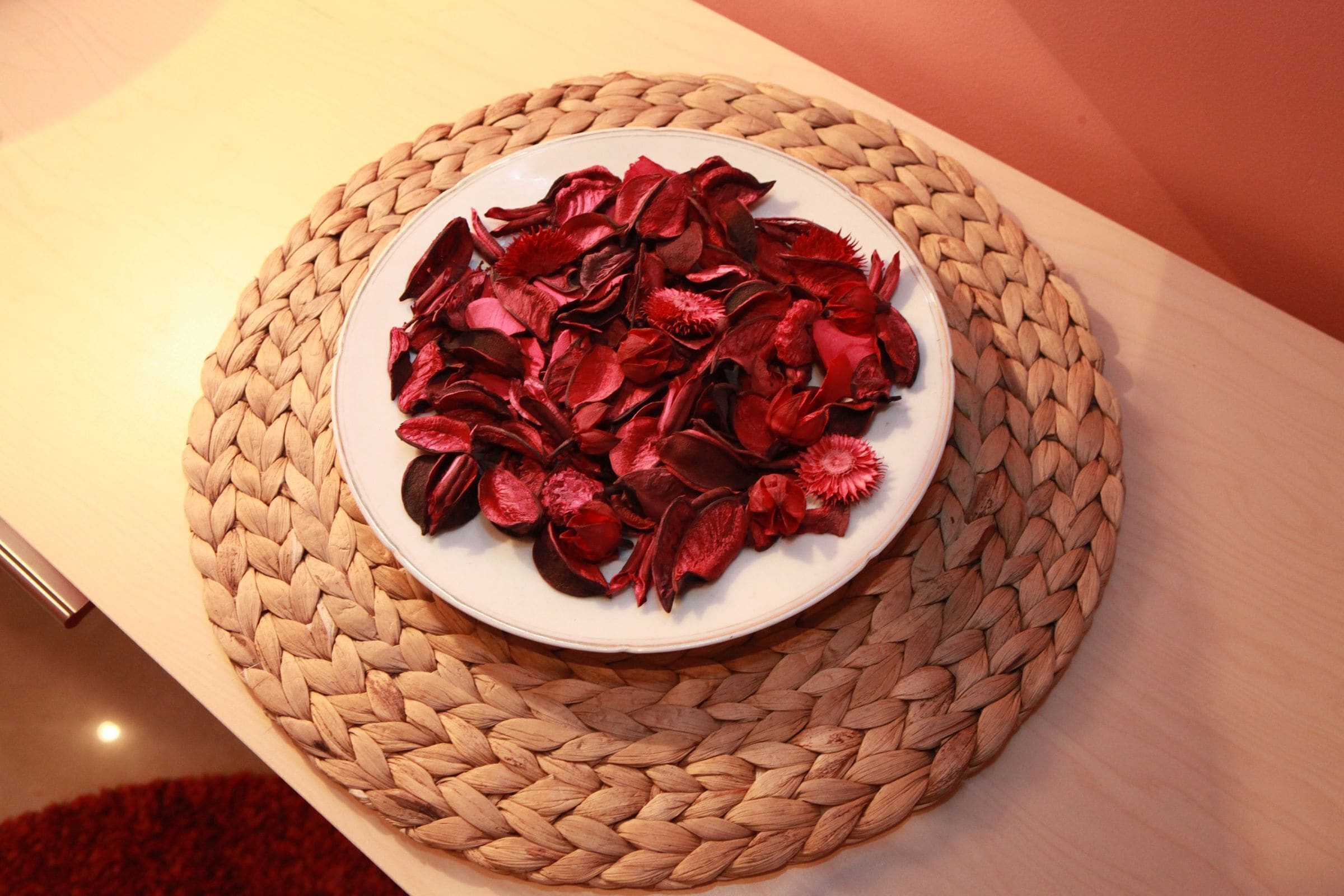 Un set de table tissé sur lequel repose une assiette remplie de fleurs rouges séchées, le tout posé sur une table en bois.