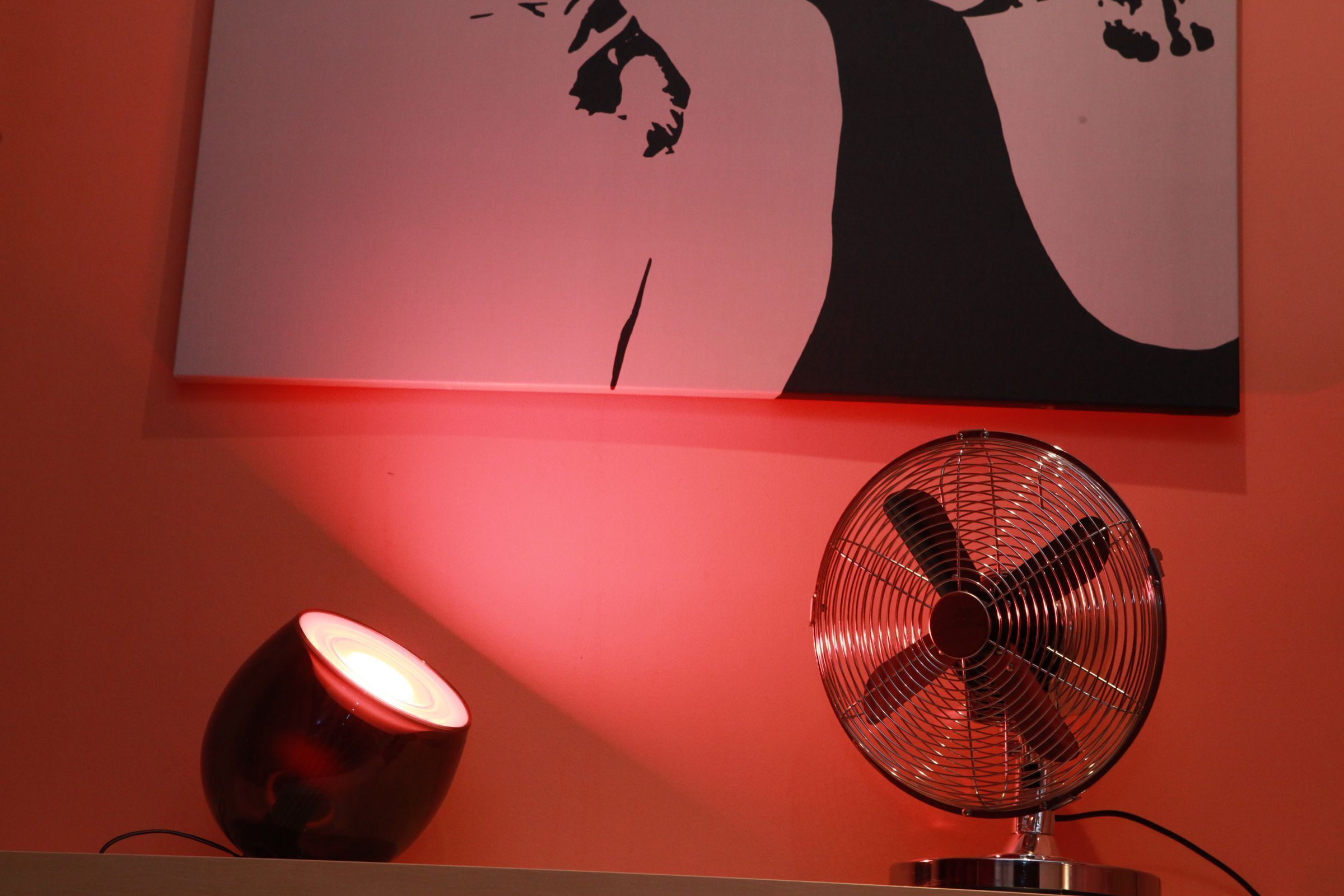 Una habitación con pared roja, techo blanco y suelo rojo. Hay un ventilador rojo y una lámpara roja sobre el suelo.