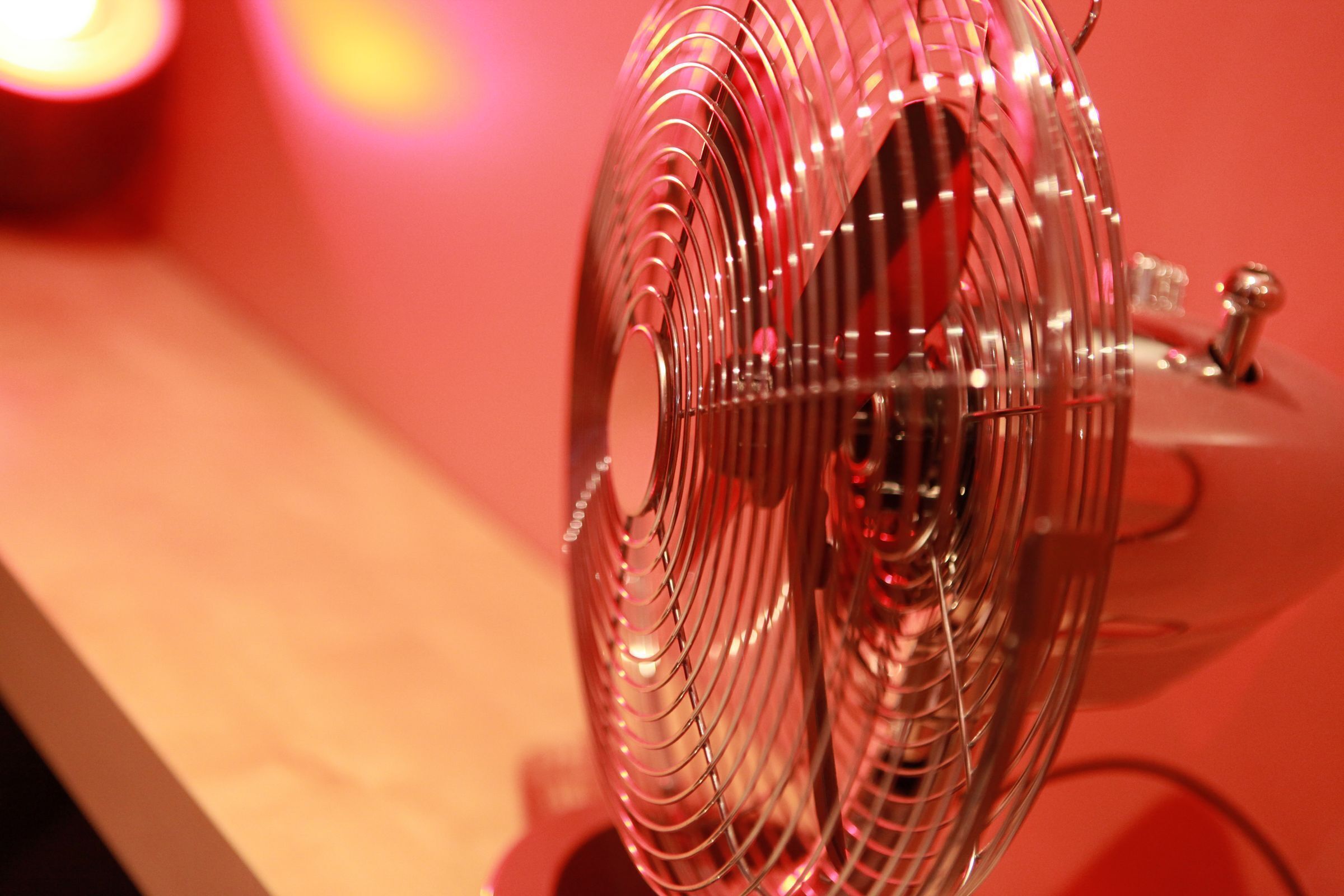 Primer plano de un ventilador metálico con superficie reflectante, sobre un fondo rojo.