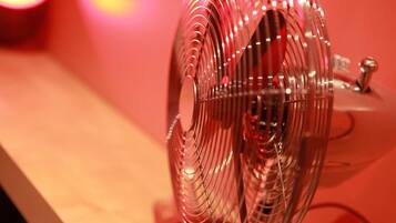 Primer plano de un ventilador metálico con superficie reflectante, sobre un fondo rojo.