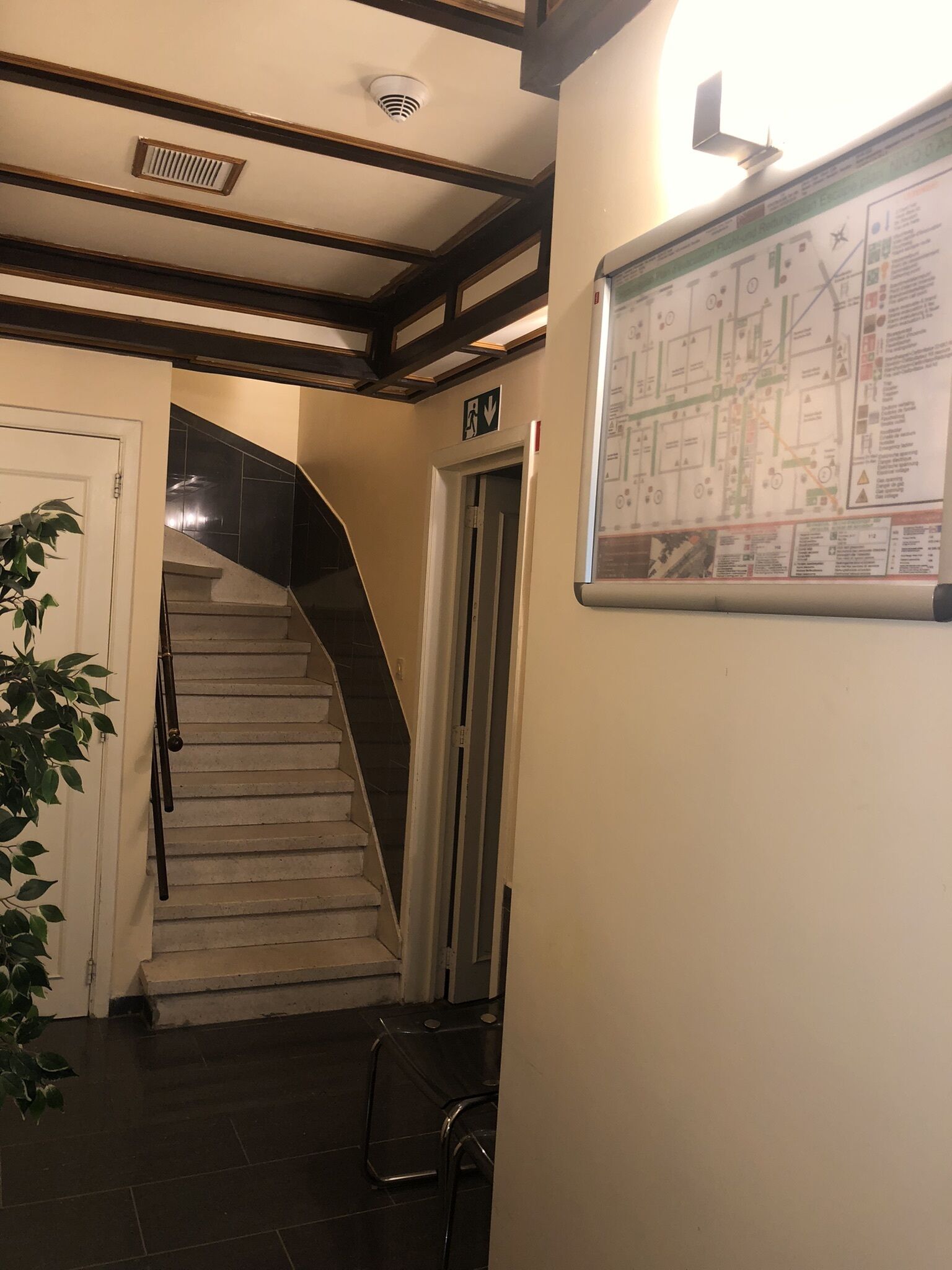 Eine Treppe mit Handlauf, eine Tür mit Notausgangsschild und eine an der Wand befestigte Karte.