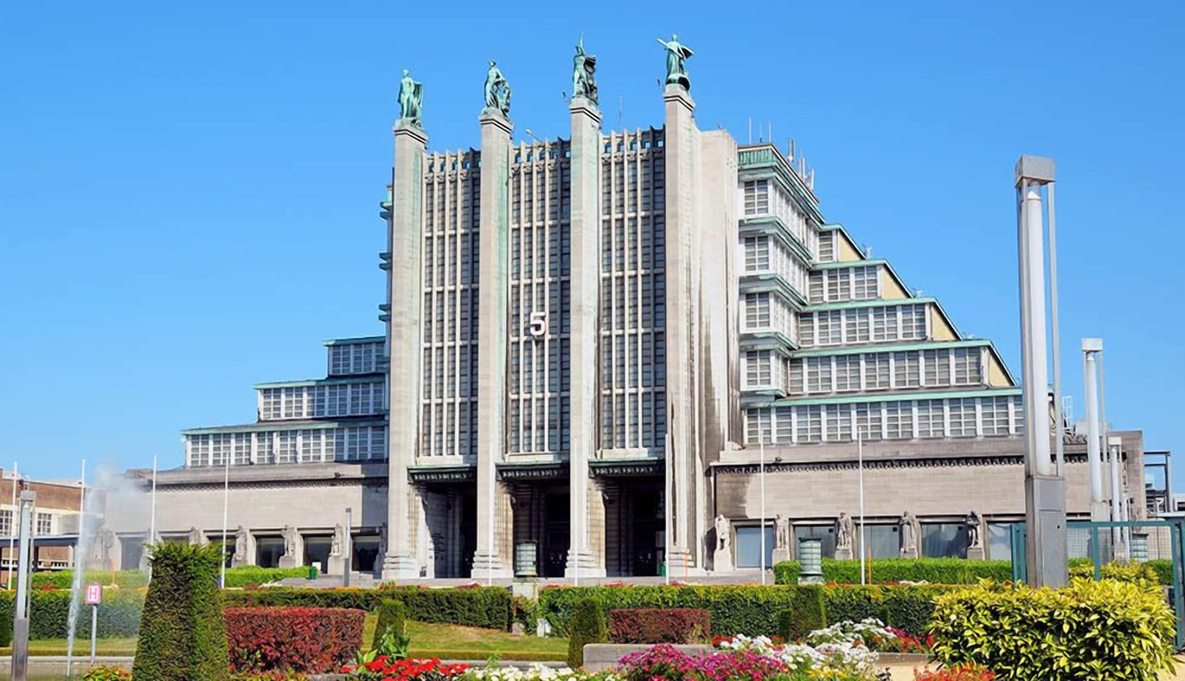 Un edificio grande de varios pisos con un diseño arquitectónico moderno, que presenta una serie de columnas verticales y estatuas en la fachada.