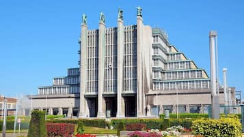 Un edificio grande de varios pisos con un diseño arquitectónico moderno, que presenta una serie de columnas verticales y estatuas en la fachada.
