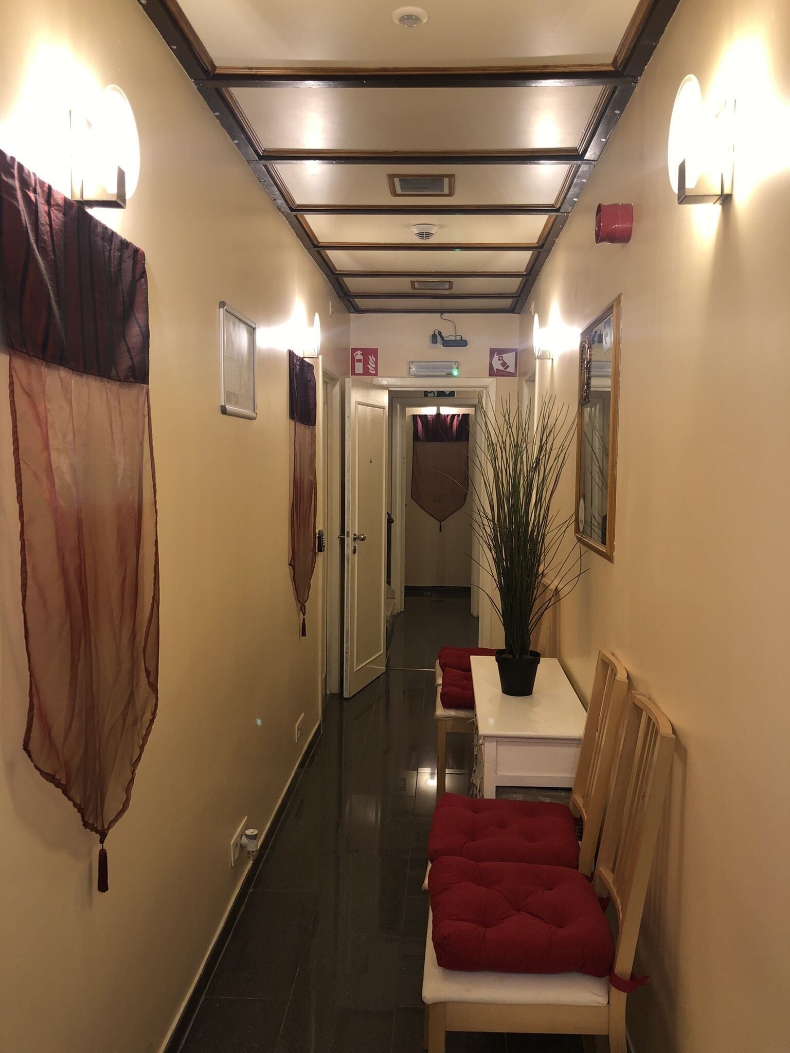 Un pasillo de hotel con una lámpara en el techo, una planta en maceta y un banco acolchado rojo.