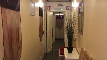 Un pasillo de hotel con una lámpara en el techo, una planta en maceta y un banco acolchado rojo.