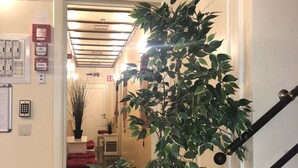 A hallway with a staircase, a potted plant, and emergency exit signs. - Residence la Fraisiere (Brussels)