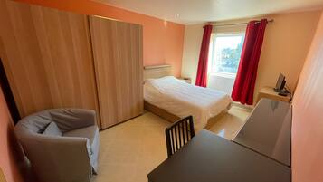 A compact hotel room with a bed, a desk, and a chair.