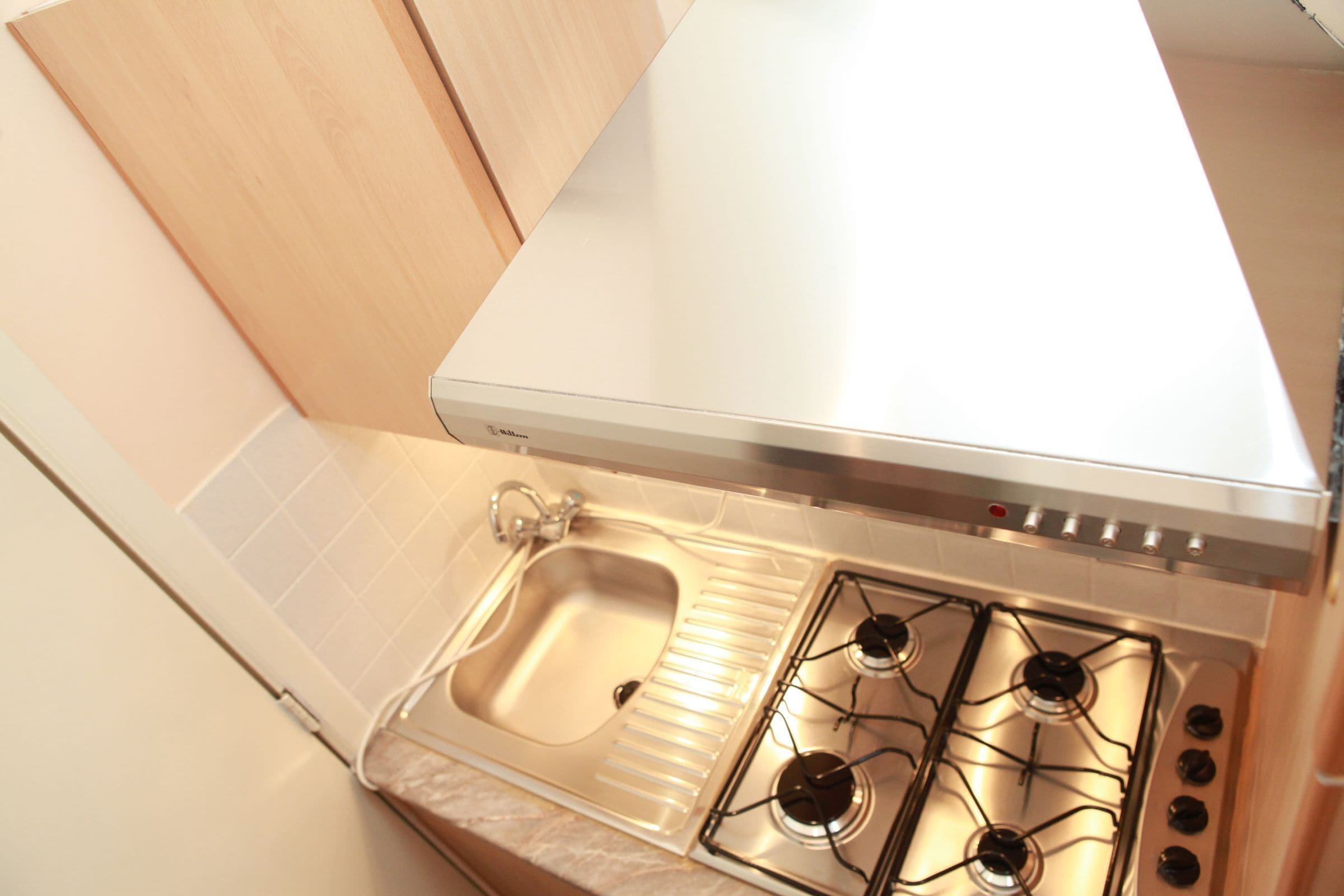 Une cuisine dotée d’un évier en acier inoxydable, d’une cuisinière à gaz avec quatre brûleurs et d’un crédence blanche.