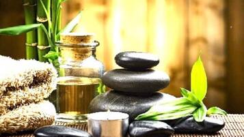 A spa setting with a bamboo backdrop, a bottle of oil, a stack of stones, a candle, and a green plant.