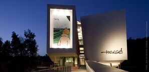 A modern building with a large illuminated sign featuring a cartoon character and the word "HERGE". - Residence la Fraisiere (Brussels)