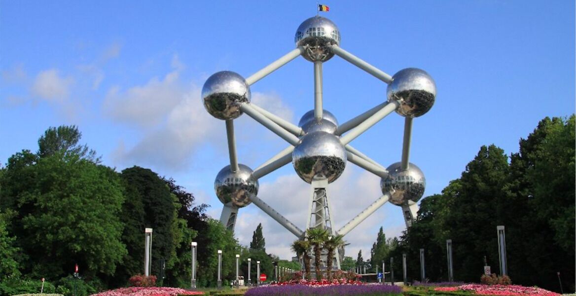 Una gran estructura metálica con varios elementos esféricos y una bandera en la parte superior, rodeada de follaje y flores.
