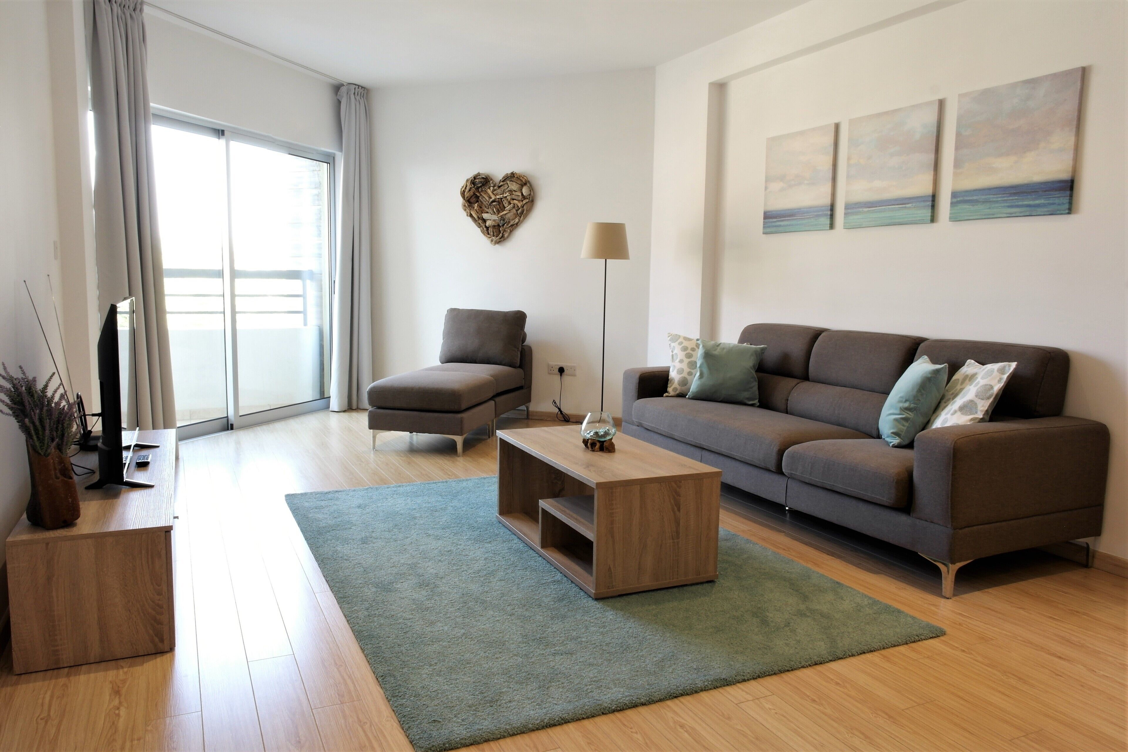 A modern living room with a sofa, armchair, coffee table, and a heart-shaped wall decoration.
